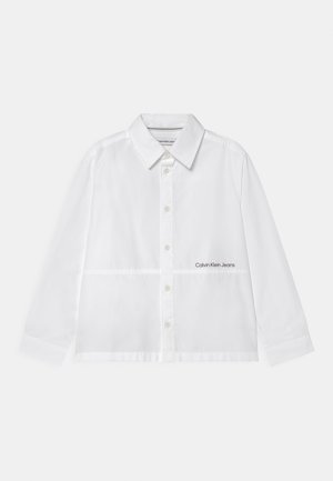 Biała koszula na guziki z długimi rękawami, zaostrzonym kołnierzykiem oraz logo "Calvin Klein Jeans" na dolnej prawej stronie.
