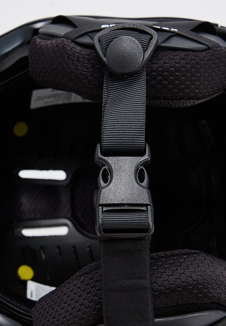 Wnętrze czarnego kasku z teksturowanym materiałem wyściełającym, regulowanymi czarnymi paskami i bezpiecznym zapięciem. Posiada otwory wentylacyjne oraz branding.