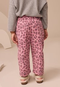 Ružové nohavice s leopardím vzorom vyrobené z mäkkej tkaniny s elastickým pásom, vybavené dvoma zadnými vreckami a voľným strihom.