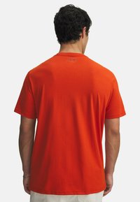 Camiseta de algodón roja de manga corta, con cuello redondo y un logo en la parte posterior, mostrada desde un ángulo trasero con una textura suave.