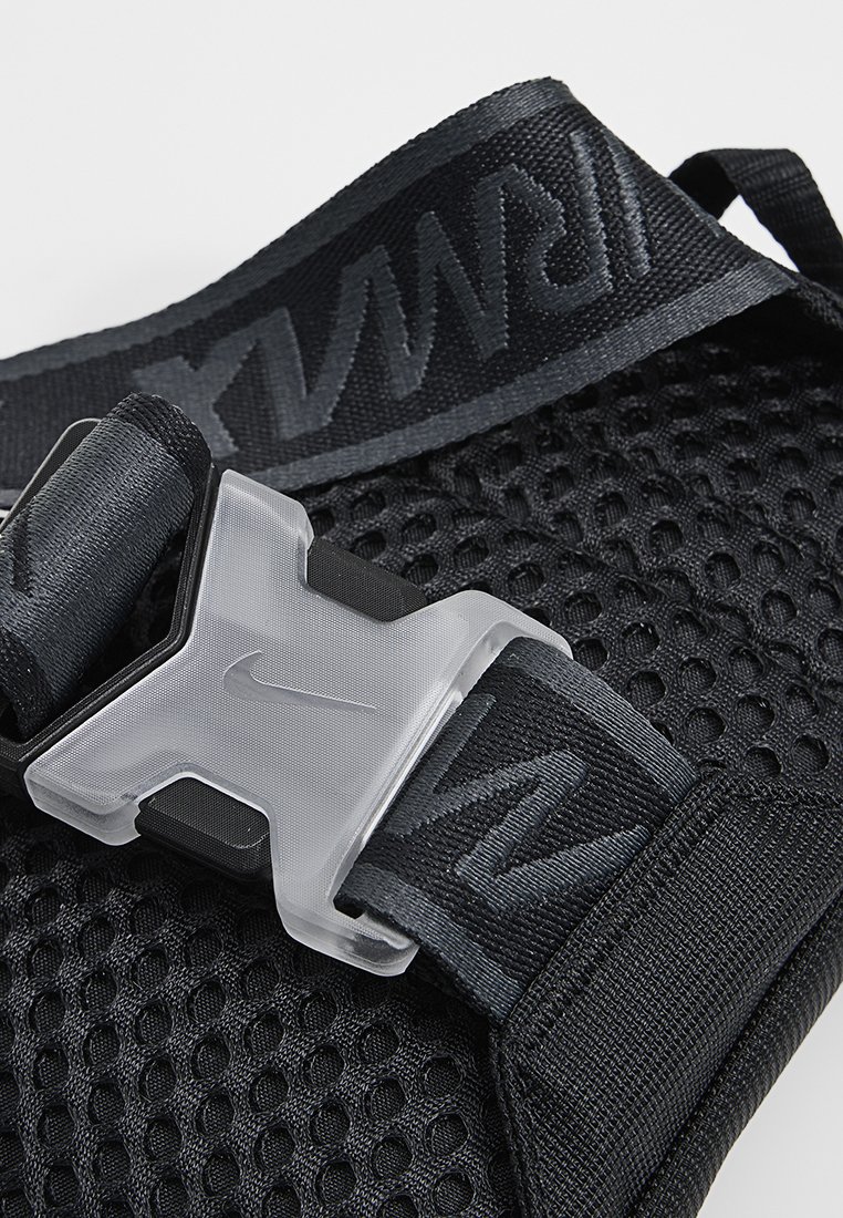 Tela de malla negra con correa negra ajustable que presenta una hebilla de plástico translúcido y el logo de Nike grabado en la correa.
