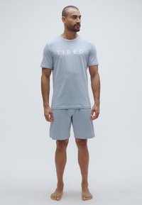 Ανοιχτό γαλάζιο κοντομάνικο μπλουζάκι με τη λέξη "Κουρασμένος" τυπωμένη μπροστά, σετ με ταιριαστό σόρτς. Απλό, λείο ύφασμα και άνετη εφαρμογή.