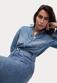 Camicia in denim di colore azzurro chiaro, con davanti a bottoni, colletto e tasca applicata. Gonna in denim a vita alta nella stessa tonalità. Texture liscia.