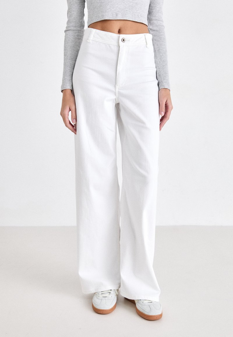 Witte wijde denimbroek met hoge taille, knoopsluiting aan de voorkant en een soepele textuur. Gecombineerd met lichte sneakers.