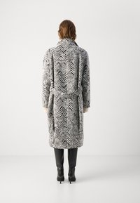 Abrigo de pata de gallo en blanco y negro con cintura ceñida, mangas largas y bolsillos laterales, combinado con botas negras hasta la rodilla.