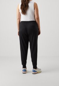 Černé joggingové kalhoty s tapered střihem a žebrovanými manžetami, doplněné bílým tílkem a barevnými sportovními botami.