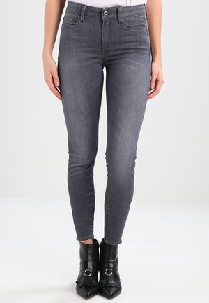 Jeans ajustados grises de denim, con un clásico diseño de cinco bolsillos y una sutil textura desgastada. Combinados con botas negras de tacón.