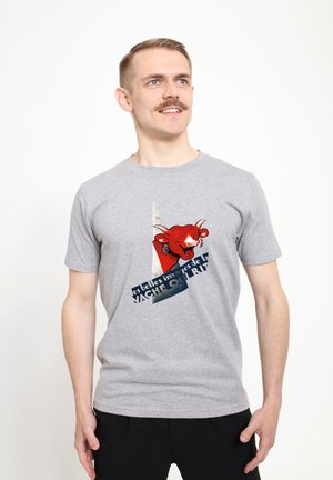 Šedé tričko s krátkým rukávem, které zobrazuje barevnou grafiku krávy a text. Materiál je hladký a volně střižený. Jednoduché pozadí.
