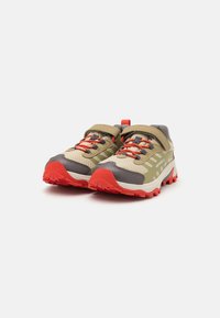 Zapatillas de trail ligeras con parte superior de malla en marrón claro y gris, acentos rojos y una suela de goma roja resistente para tracción. Cierre con correa ajustable.