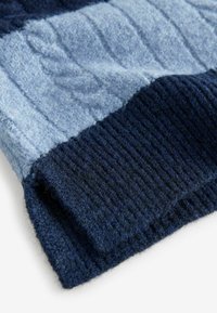 Svetr z vlny s texturovaným vzorem kabelového pletení v odstínech modré a námořnické modři, s žebrovaným lemem a měkkou, chlupatou texturou.