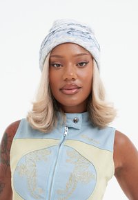 Blue and white textured beanie with a wavy pattern. Worn with a sleeveless, zippered, blue and green top featuring embroidered tiger details.
