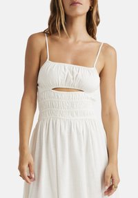 Abito bianco con spalline sottili, tessuto arricciato e dettaglio con cut-out in vita, caratterizzato da una gonna fluida e un tessuto leggero.