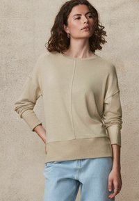 Maglione lavorato a maglia color beige chiaro con scollo rotondo, polsini e orlo a costine. Presenta un design a spacco sul davanti e una texture morbida.