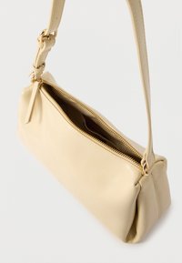 Sac à main rectangulaire beige avec une bandoulière unique et une fermeture éclair dorée partiellement ouverte sur un fond blanc.