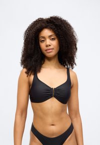 Černý horní díl bikin s nařaseným středem a zlatými kovovými ozdobami, širokými ramínky a hladkou texturou, ve spojení s odpovídajícími spodními díly.