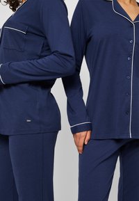 Mörkblå pyjamas-set i mjukt tyg, med långa ärmar, knappstängning fram, vit pipingskant och sidfickdetalj på toppen.