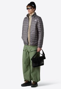 Šedá péřová bunda, zelené kalhoty širokého střihu, béžový fleecový top, černá taška, sluneční brýle a čepice. Texturovaná tkanina a různé odstíny.