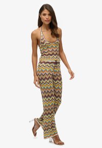 Haut en halter à motif zigzag multicolore et pantalons assortis, fabriqués en tissu léger. Accentués par une taille à cordon et des jambes évasées.
