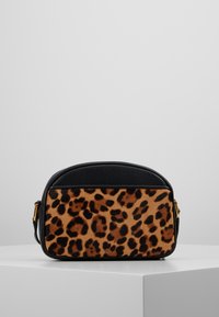 Kabelka s leopardím vzorem, černými hrubými koženými akcenty, zlatou kováním a zaobleným tvarem. Hladký povrch s výraznými vzory.