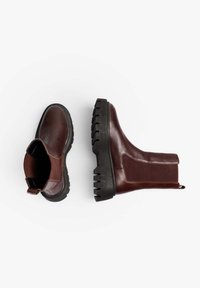 Botas de tobillo de cuero marrón con paneles elásticos en los laterales, puntera redonda y suelas de goma negra texturizadas con profundos tacos.