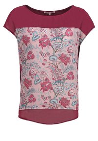 Haut à manches courtes avec un motif floral en rose et bleu sarcelle sur un fond clair, dos uni couleur bordeaux et col rond.