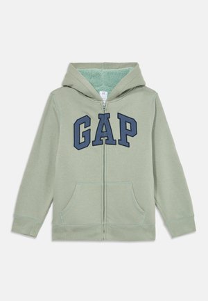 Sweat à capuche zippé vert clair avec des lettres bleues "GAP" sur la poitrine, des poches avant et une doublure intérieure en peluche dans la capuche.