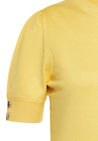 Suéter amarillo de punto con mangas cortas abullonadas, textura acanalada y detalles de botones plateados en los puños de las mangas. Tejido suave y ligero.