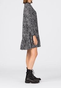 Blommönstrad, marinblå klänning med långa ärmar och volangkant, i kombination med svarta snörboots. Slät tygtextur.