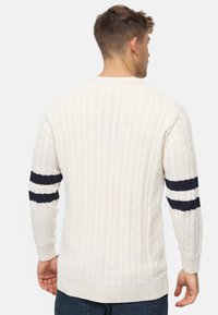 Kabelstrikket sweater i kremfarve med marineblå striber på ærmerne. Har ribbede manchetter og kant, som fremhæver teksturerede mønstre.