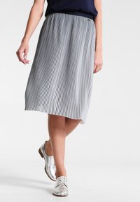 Middihame, jossa on mustavalkoisia poimutuksia ja elastinen vyötärö. Yhdistetty hopeisiin nauhallisiin kenkiin, jotka esittelevät sileää pintaa.