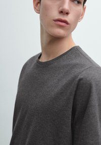 Szary bawełniany T-shirt z okrągłym dekoltem, miękką fakturą i krótkimi rękawami, pokazany z boku. Minimalistyczny design.