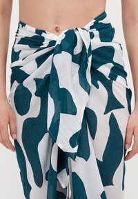 Jupe en coton de couleur bleu foncé et blanche avec un motif abstrait, dotée d'un détail noué à la taille et d'un tissu léger et texturé.