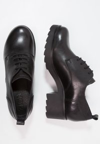 Svarta läder snörskor med kraftiga klackar och räfflade sulor, visade från ovan och sidan på en vit bakgrund.