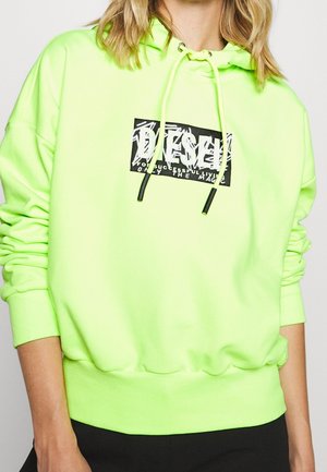 Neon zelená mikina s kapucí, se stahovací šňůrkou, žebrovanými manžetami a pasem. Na přední straně má grafickou nášivku loga v černé a bílé barvě.