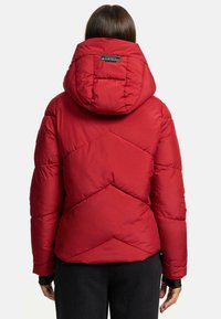 Doudoune rouge isolée avec capuche, présentant un motif en diamant et des poignets élastiques. Logo au dos près du col. Texture lisse.