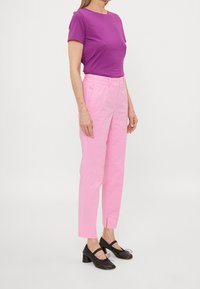 Paarse t-shirt met korte mouwen, lichte stof; roze rechte broek met front pockets; zwarte schoenen met een bandje en blokhak.