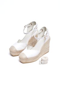 Alpargatas blancas con cuña y suela de yute trenzado, con lados abiertos y una puntera beige. Incluyen una correa de tobillo a juego y una cinta de tela.