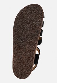 Schwarze Korksohlen-Sandale mit einer strukturierten braunen Gummisohle, verstellbaren schwarzen Riemen und einem konturierten Fußbett für Komfort.