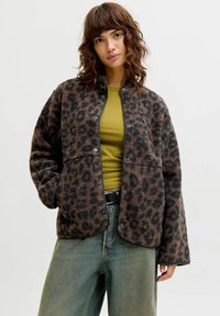 Leopardmønstret fleecejakke i brunt og svart med knappelukking foran, lange ermer og en avslappet passform, kombinert med en grønn topp og denim.