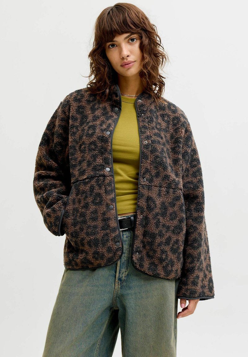 Leopardmønstret fleecejakke i brunt og svart med knappelukking foran, lange ermer og en avslappet passform, kombinert med en grønn topp og denim.