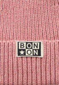 Tessuto di maglia rosa con un'etichetta rettangolare nera e bianca che presenta il testo "BON*ON" in lettere maiuscole.