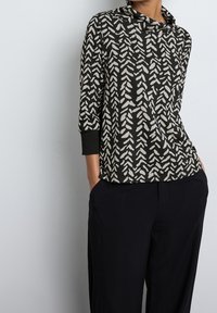 Hnědo-černý vzorovaný top s výstřihem do cowl, tříčtvrtečními rukávy a volným střihem; měkká tkanina s geometrickým listovým vzorem.