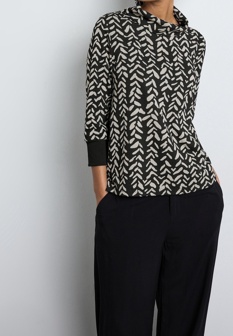 Hnědo-černý vzorovaný top s výstřihem do cowl, tříčtvrtečními rukávy a volným střihem; měkká tkanina s geometrickým listovým vzorem.