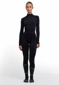 Czarna bluzka z długim rękawem z zamkiem z przodu, zestawiona z czarnymi legginsami i szarymi skarpetami do kolan z białymi akcentami. Gładka tekstura na całej powierzchni.