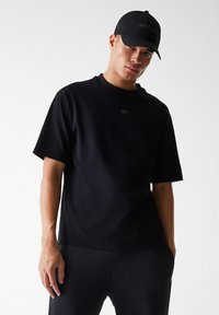 Black short-sleeve t-shirt with a crew neck, made of smooth fabric, featuring a small logo detail on the chest and paired with black athletic pants.