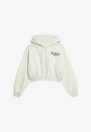 Sudadera corta gris claro hecha de tela suave, con cremallera frontal, dobladillo acanalado y texto impreso que dice "THE BRONX N.Y.C." en el pecho.