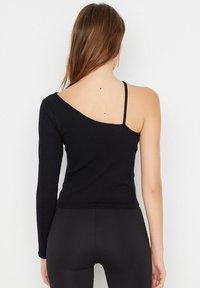 Svart ribbad långärmad topp med en asymmetrisk design, en axelrem och en hel ärm. Mjuk textur och figurnära silhuett.