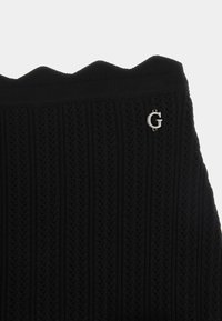 Suéter negro de punto con textura acanalada y dobladillo en forma de ondas. Presenta un pequeño acento con el logo plateado "G" en el lado izquierdo.