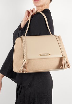 Beige håndtaske med tekstureret stof og glat læder, med flettede detaljer og frynser, guldbelægning og et struktureret design.