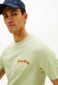 Lys grøn bomuld t-shirt med korte ærmer og rund halsudskæring, med rødt broderet "Tommy HILFIGER" logo på brystet.